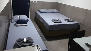 A small, compact room with two single beds, a desk, and a chair.