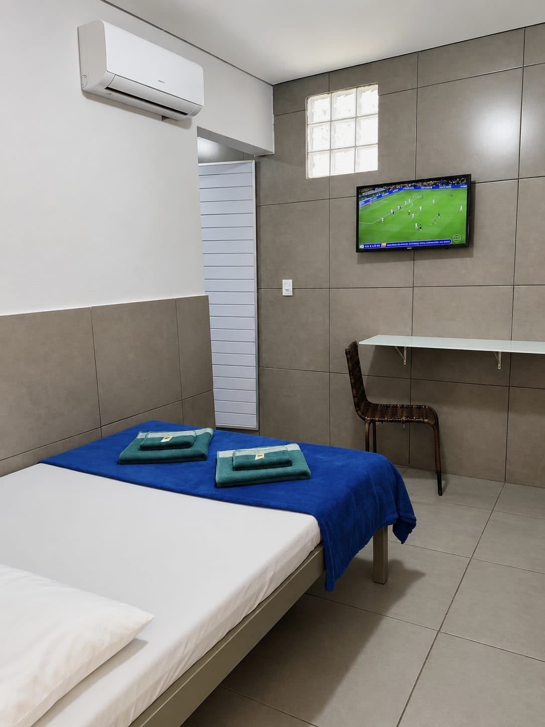 Quarto de hotel com cama, televisão na parede e janela.