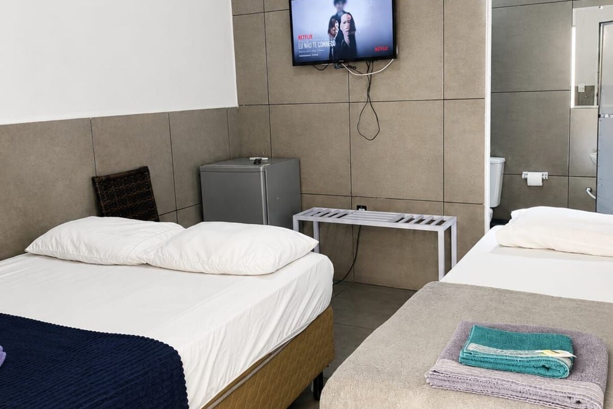 A hotel room with two beds, a television mounted on the wall, a small desk, and an air conditioning unit.