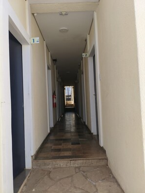 Un pasillo con puertas numeradas, un extintor y suelo de baldosas.