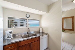 A kitchen with a stainless steel sink, a coffee maker, a dishwasher, and a window with blinds. - Gorgeous Ocean Views in the Heart of Waikiki! Full Kitchen, Free Wi-Fi & More (Honolulu)