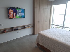 Ein Schlafzimmer mit einem Bett, einem an der Wand montierten Fernseher, einem Kleiderschrank und einem Fenster mit Aussicht.