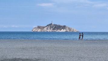 Une plage avec une île rocheuse à l’horizon et deux personnes debout sur le sable.