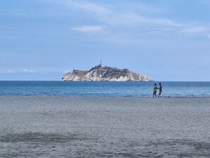 Ein Strand mit einer Felseninsel in der Ferne und zwei Personen, die am Sand stehen.