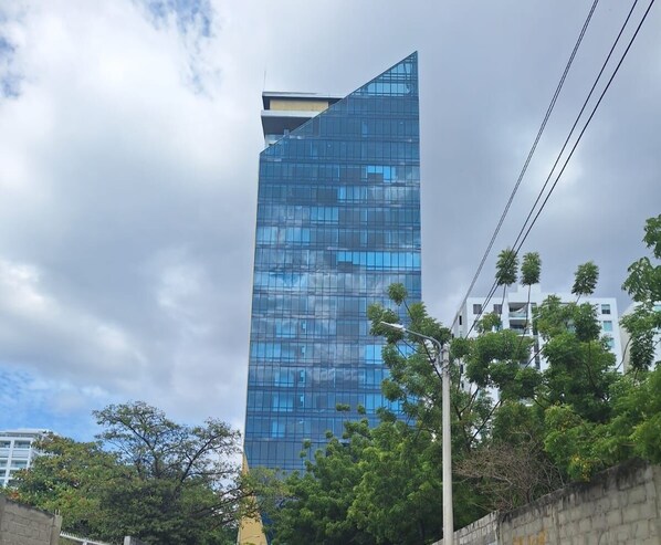 Ein modernes Glasgebäude mit einem markanten, winkligen Design, umgeben von Bäumen und blauem Himmel.
