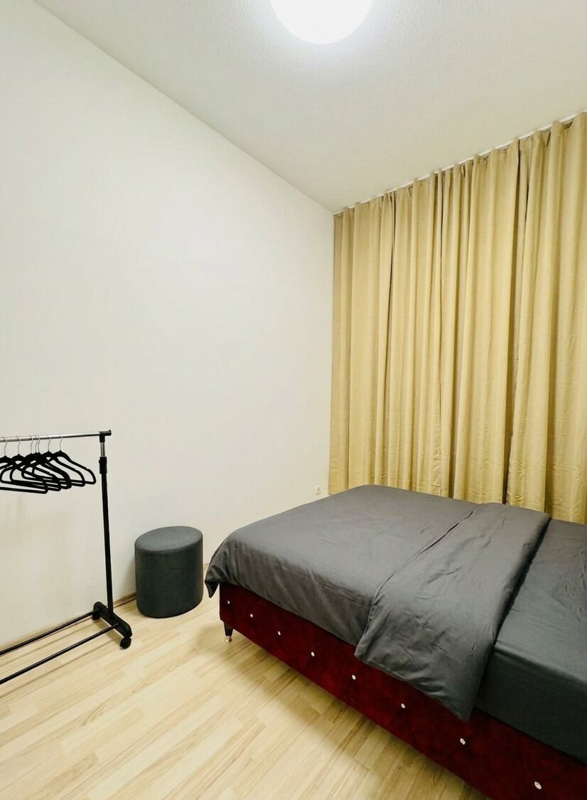 A bedroom with a bed, a clothing rack, a cylindrical object, and curtains.
