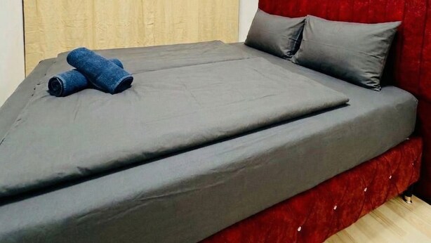 A single bed with a grey mattress and red headboard, a pair of rolled-up blue towels, and beige curtains on a white wall. - Cozy Room Near FAC Platz (Vienna)