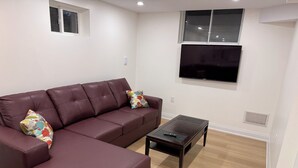 A living room with a sectional sofa, a coffee table, and a flat-screen TV mounted on the wall. - Modern Legal Basement Suite with Separate Entrance (Mississauga)