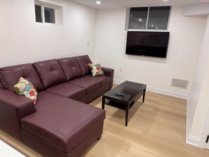 A living room with a sectional sofa, a coffee table, and a flat-screen TV mounted on the wall. - Modern Legal Basement Suite with Separate Entrance (Mississauga)