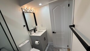 A bathroom with a toilet, sink, mirror, and a door. - Modern Legal Basement Suite with Separate Entrance (Mississauga)