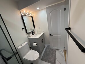 A bathroom with a toilet, sink, mirror, and a door. - Modern Legal Basement Suite with Separate Entrance (Mississauga)