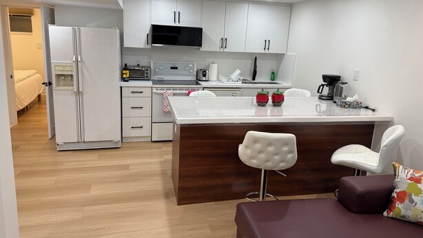 A modern kitchen with white cabinets, a microwave, a toaster, and a coffee maker. There is a wooden dining table with two white chairs. - Modern Legal Basement Suite with Separate Entrance (Mississauga)
