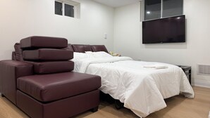 A modern bedroom with a bed, a sofa, a TV, and a window. - Modern Legal Basement Suite with Separate Entrance (Mississauga)