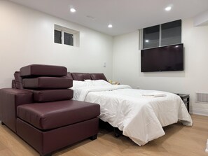 A modern bedroom with a bed, a sofa, a TV, and a window. - Modern Legal Basement Suite with Separate Entrance (Mississauga)