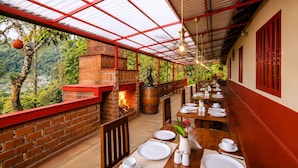 Un restaurante con chimenea de ladrillo, mesas al aire libre y vistas a la vegetación circundante.