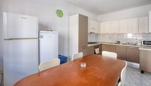 Une cuisine compacte avec des meubles blancs, une table à manger en bois et un petit réfrigérateur.