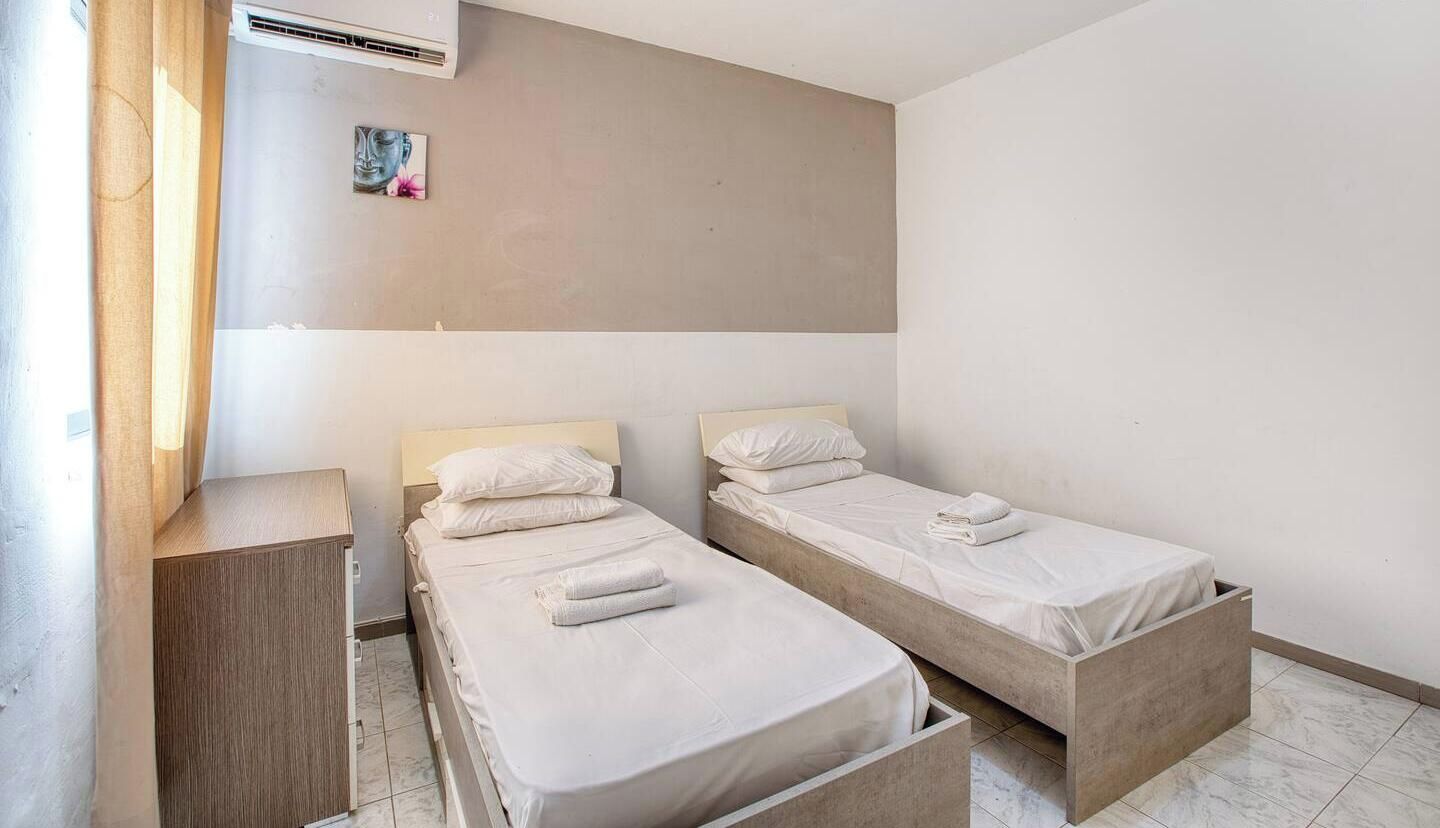 A room with two single beds, a wooden cabinet, and a wall-mounted air conditioner.