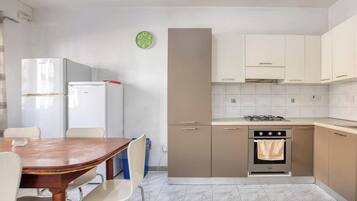 Una cucina compatta con zona pranzo, frigorifero, fornello e orologio a parete.