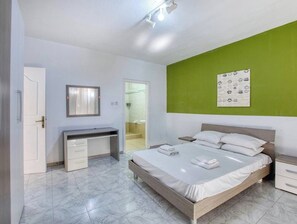 Une chambre à coucher avec un lit, des tables de chevet, un bureau et une porte menant à la salle de bain.