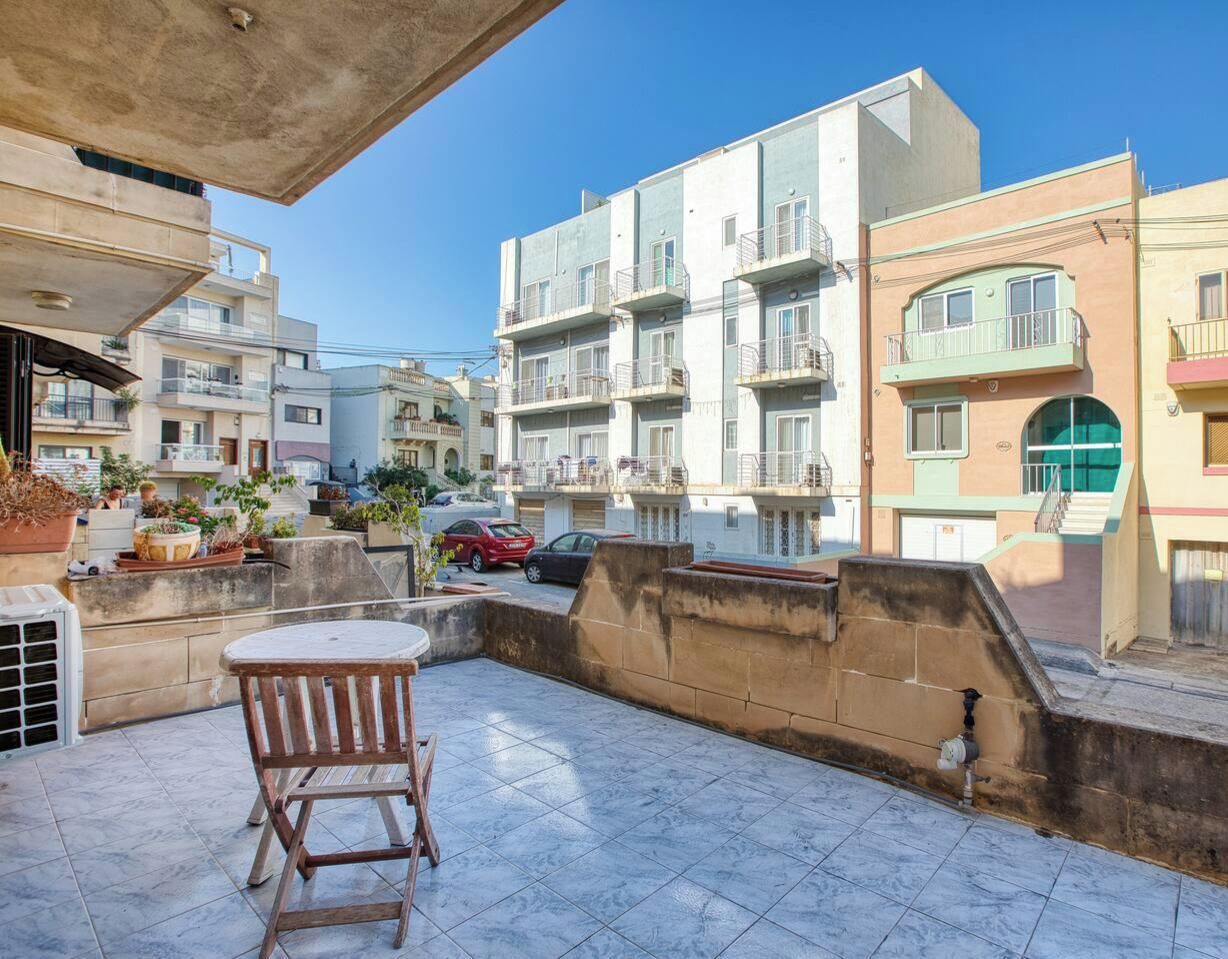 Un immeuble résidentiel doté de nombreux balcons, d’une terrasse carrelée et d’une voiture garée.