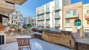 Un immeuble résidentiel doté de nombreux balcons, d’une terrasse carrelée et d’une voiture garée.
