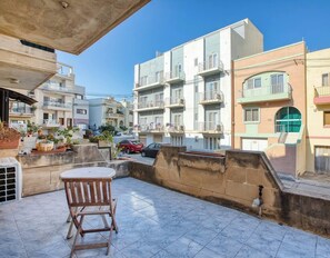 Un immeuble résidentiel doté de nombreux balcons, d’une terrasse carrelée et d’une voiture garée.