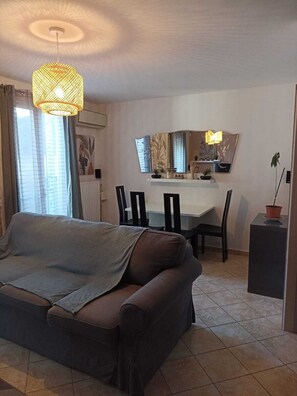 A living room with a sofa, a dining table with chairs, a hanging light fixture, a mirror, and a radiator. - House for 8 people •Jacuzzi Spa• Garden• Parking • Air Conditioning (Avignon)