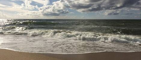 A beach with waves approaching the shore under a partly cloudy sky.