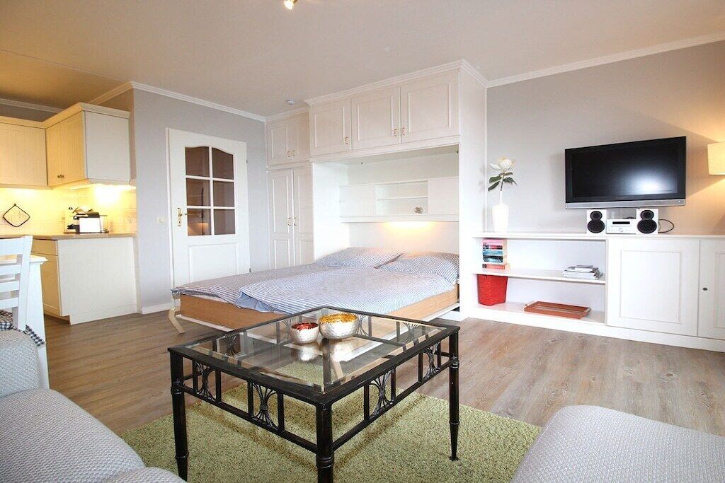 Ein kompakter Wohnbereich mit Bett, Glastisch, Fernseher und einer Küchenzeile.