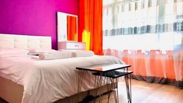 Ein Schlafzimmer mit einem Bett, einem Nachttisch, einem Spiegel und einem Fenster mit Vorhängen.