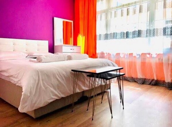 A bedroom with a bed, a bedside table, a mirror, and a window with curtains. - hilltop hostel (fatih istanbul)