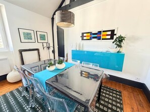 A modern dining area with a glass table, clear chairs, and a blue tablecloth. There is a blue cabinet with decorative items on top. - Loft'Art - A one-of-a-kind loft in the heart of Vannes (Vannes)