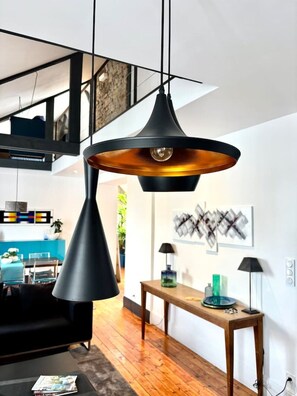 A modern living space with a black pendant light, a wooden dining table, and a kitchen in the background. - Loft'Art - A one-of-a-kind loft in the heart of Vannes (Vannes)
