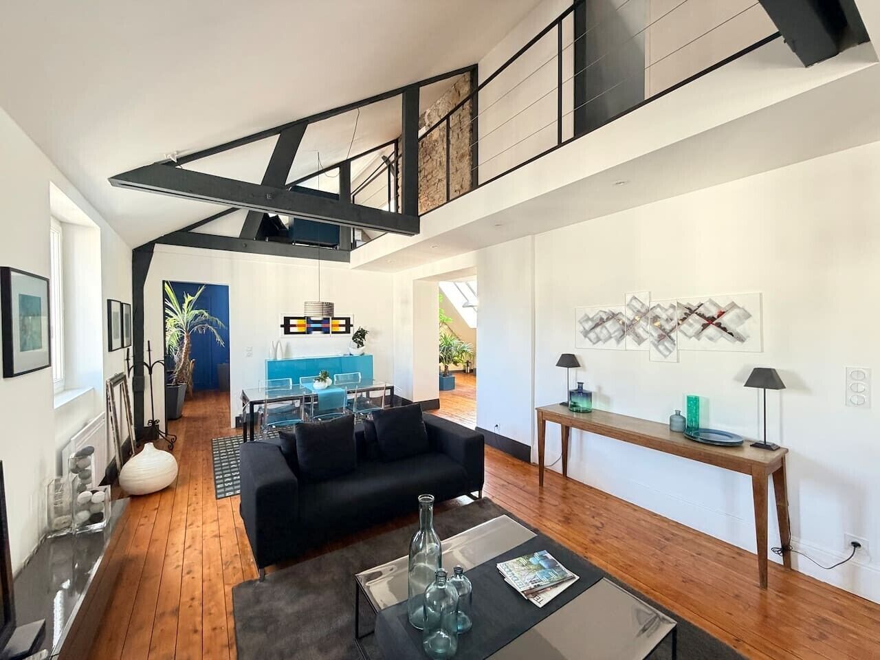 A modern interior with a black sofa, wooden flooring, a dining area with a blue table, and a staircase.