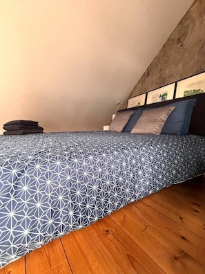 A bedroom with a geometric-patterned bedspread, a stack of folded blankets, and a wooden floor. - Loft'Art - A one-of-a-kind loft in the heart of Vannes (Vannes)