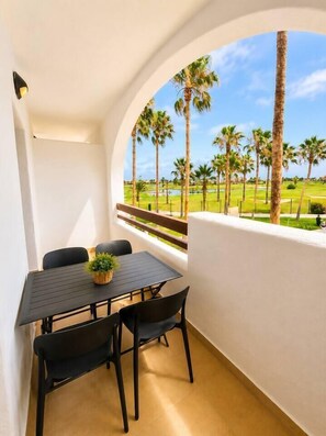 A balcony with a table and chairs, overlooking a golf course with palm trees. - Vrbo Property (Alcazares, Los)