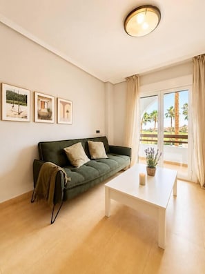 A room with a green sofa, a white coffee table, and a window with curtains. - Serena Golf Views • Beach & Golf Apartment (Alcazares, Los)