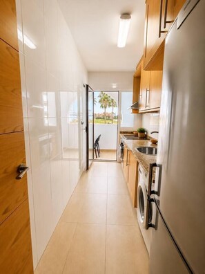 A narrow kitchen with a washing machine, a refrigerator, and a sink. - Serena Golf Views • Beach & Golf Apartment (Alcazares, Los)