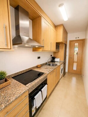 A compact kitchen with wooden cabinets, a built-in stove, a washing machine, and a refrigerator. - Serena Golf Views • Beach & Golf Apartment (Alcazares, Los)