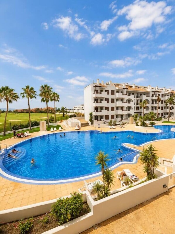 A hotel with a large swimming pool surrounded by palm trees and a golf course in the background. - Vrbo Property (Alcazares, Los)