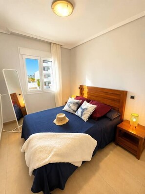 A bedroom with a bed, bedside tables, a mirror, and a window. - Vrbo Property (Alcazares, Los)