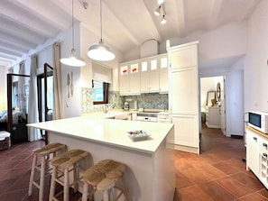 A modern kitchen with a central island, bar stools, and white cabinetry. - Designed rustic house with glazed porch and pool (Huércal-Overa)