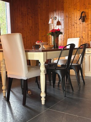 Ruokailutila, jossa on puinen seinä, pöytä ja tuolit, maljakko kukkineen ja ikkuna.