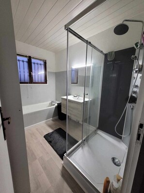 Ein modernes Badezimmer mit einer gläsernen Duschkabine, einer Badewanne und einem Waschtisch mit Spiegel.