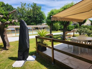 Eine Terrassenfläche mit überdachter Sitzecke, einem Pool und einem Garten.