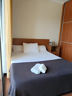 A hotel room with a bed, a nightstand, a wooden wardrobe, and a window with curtains.