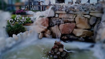Una fuente de agua con una estructura de piedra y una pequeña cascada, rodeada de follaje y flores.