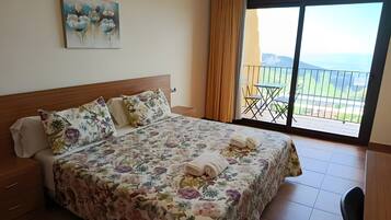Habitación de hotel con una cama grande, ropa de cama floral, un cuadro en la pared y un balcón con vistas.
