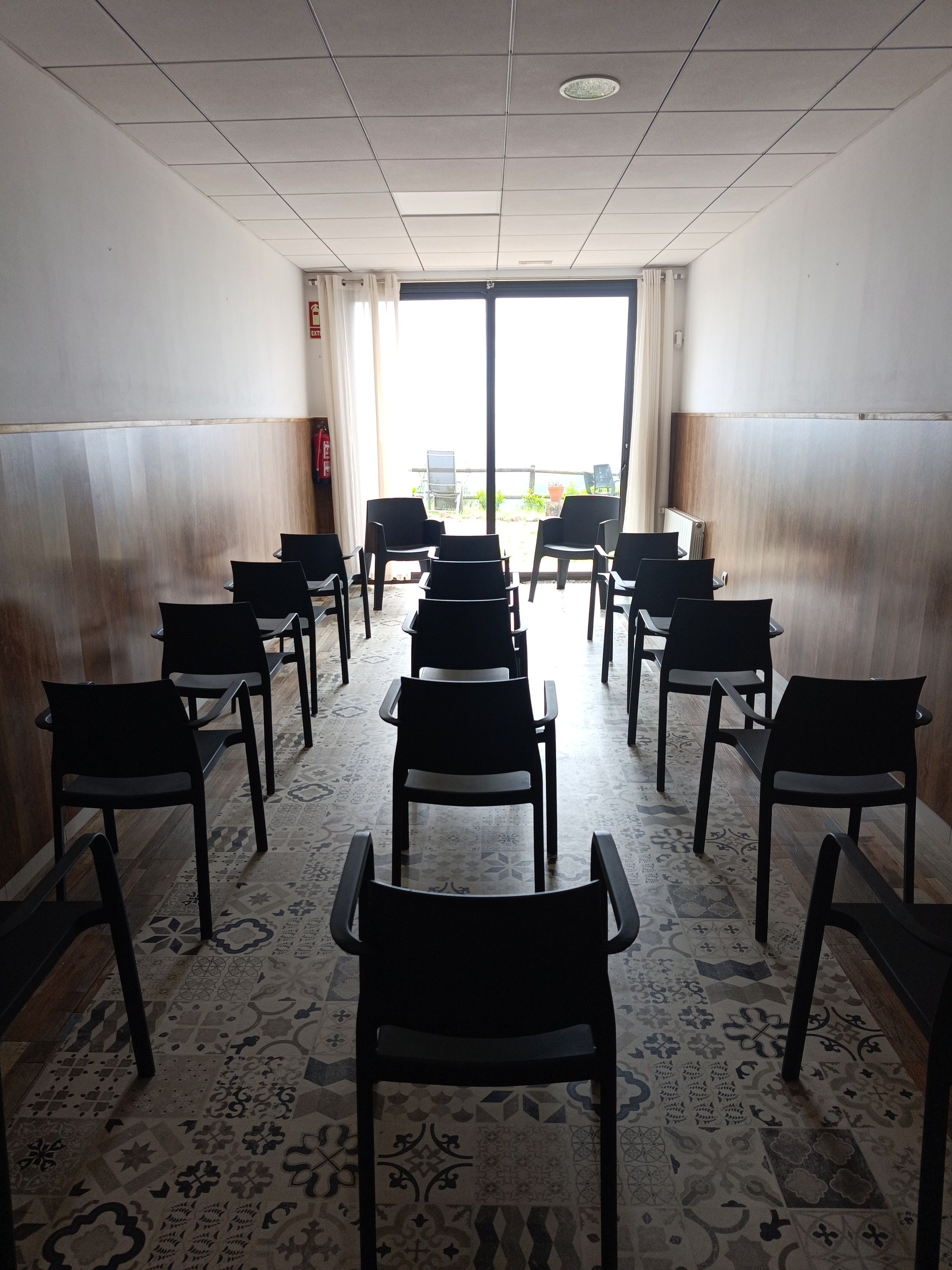 Een congreszaal met rijen stoelen, een vloer met een patroon en uitzicht door een glazen deur.