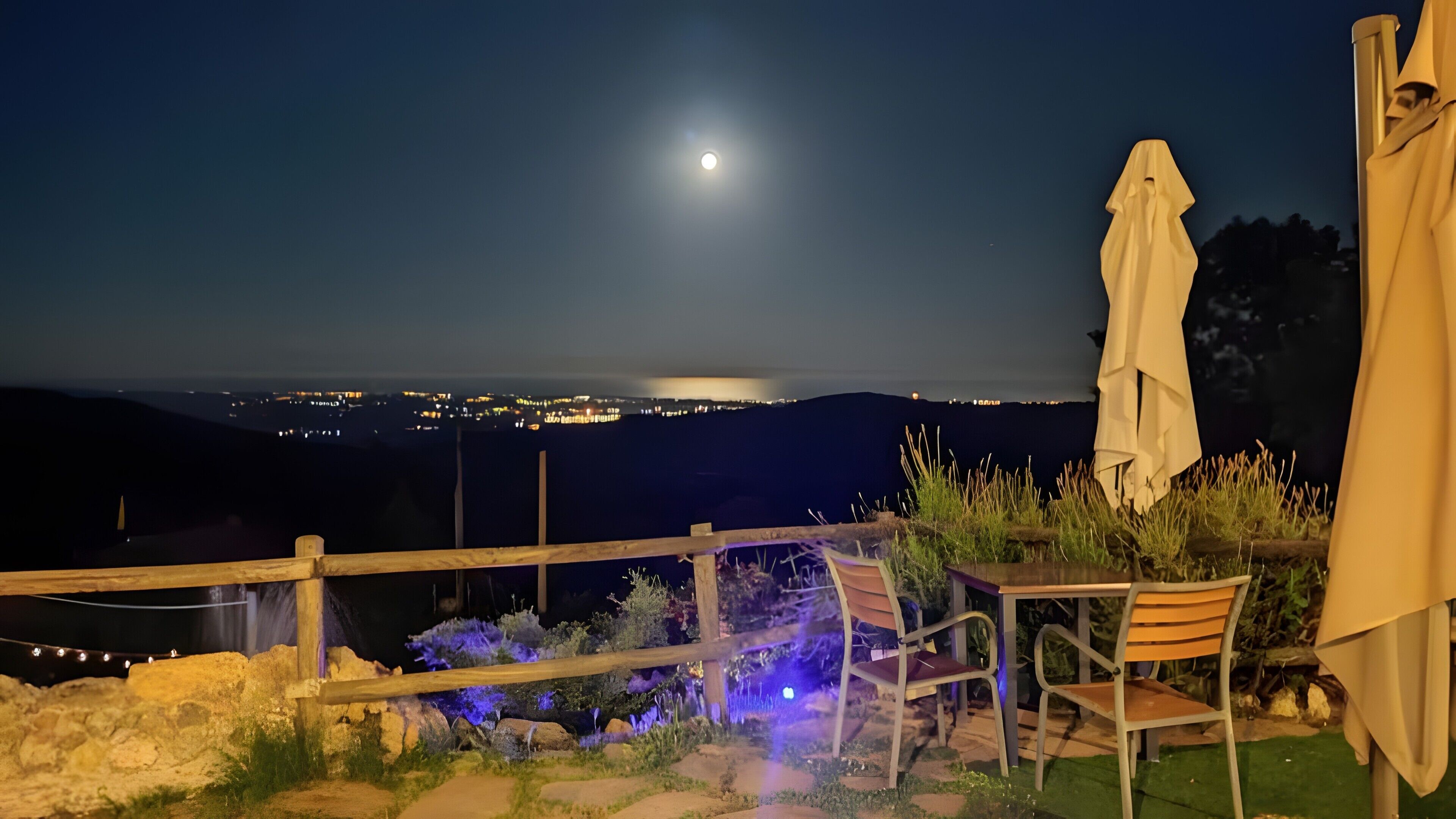 Un espace extérieur aménagé pour les soirées, avec vue sur le paysage urbain et la pleine lune.